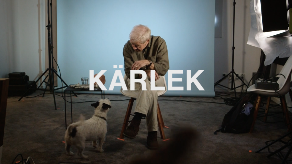 Neuropsykolog Åke Pålshammar sitter på en stol i en studio. Framför honom sitter en hund och viftar på svansen. Över bilden står ordet "Kärlek" i stora bokstäver.